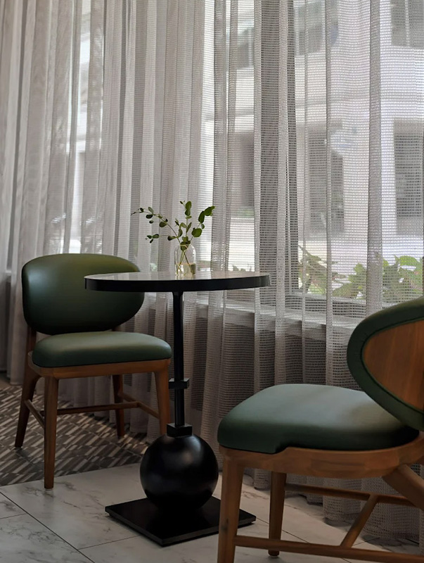 Una tranquilla area salotto dell'hotel Intercontinental con sedie imbottite verdi, un tavolino rotondo e tende trasparenti che diffondono dolcemente la luce del giorno